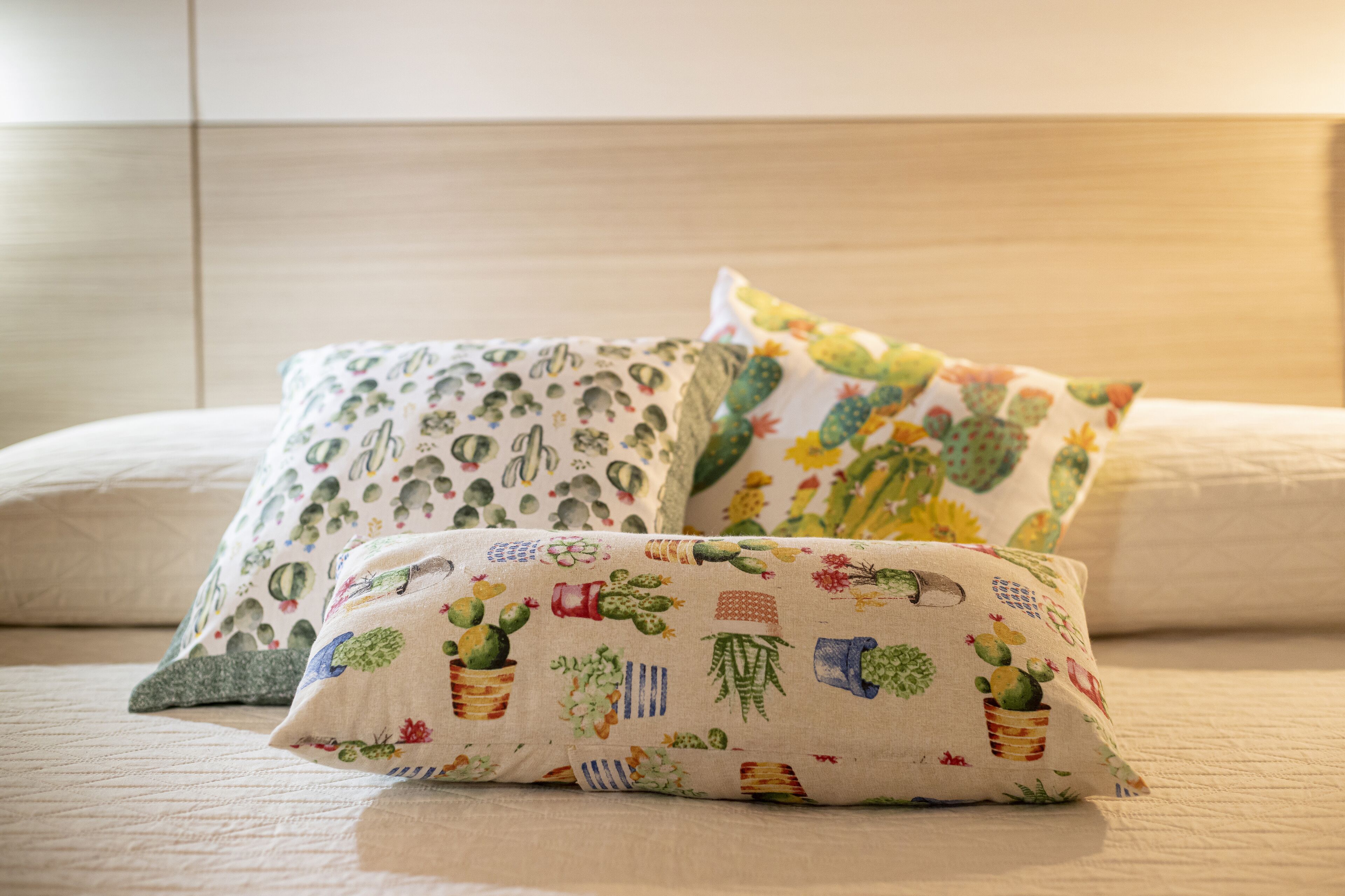 A bed with three pillows featuring cactus and desert plant patterns.