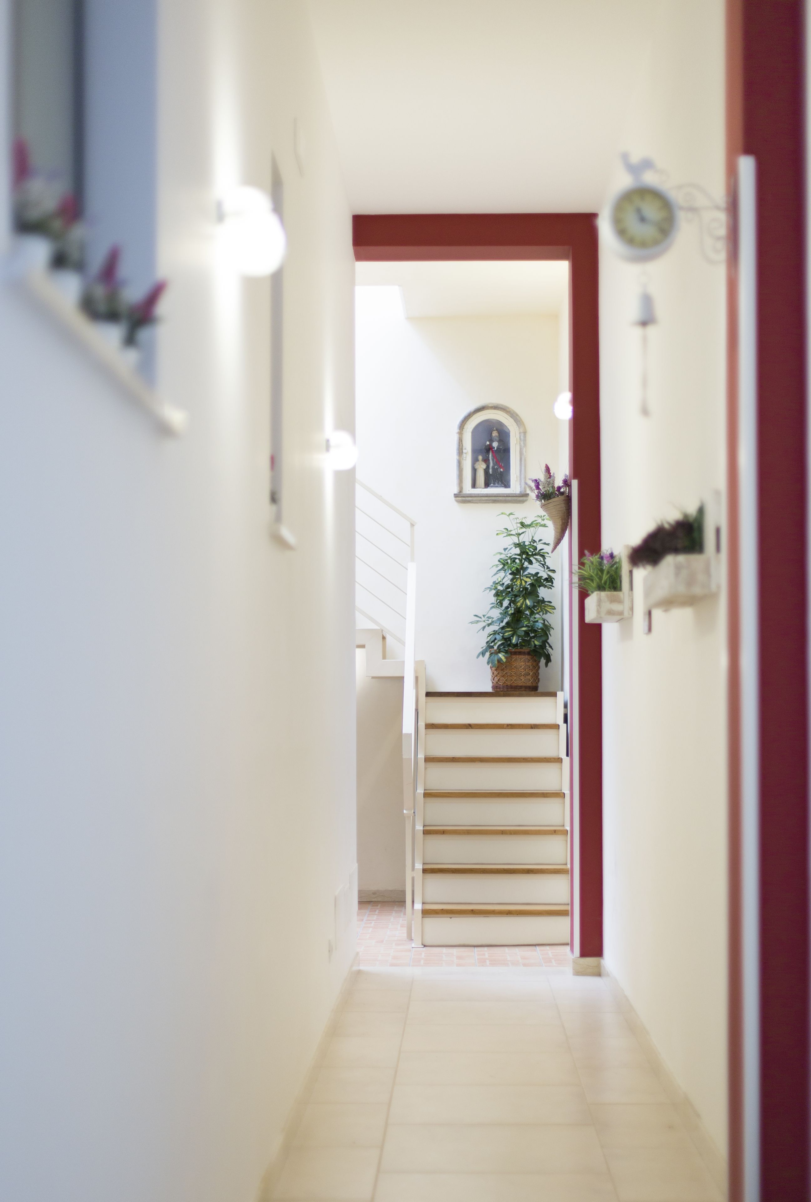 A narrow hallway with a staircase leading to a landing. There are wall-mounted light fixtures and a clock on the wall.
