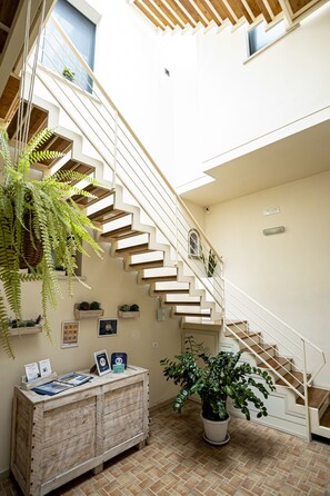 A staircase with a wooden finish, a reception desk with informational materials, and potted plants. - Trapani Home (Trapani)