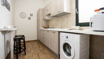 A compact kitchen with a washing machine, wooden cabinets, a sink, and a small stool.