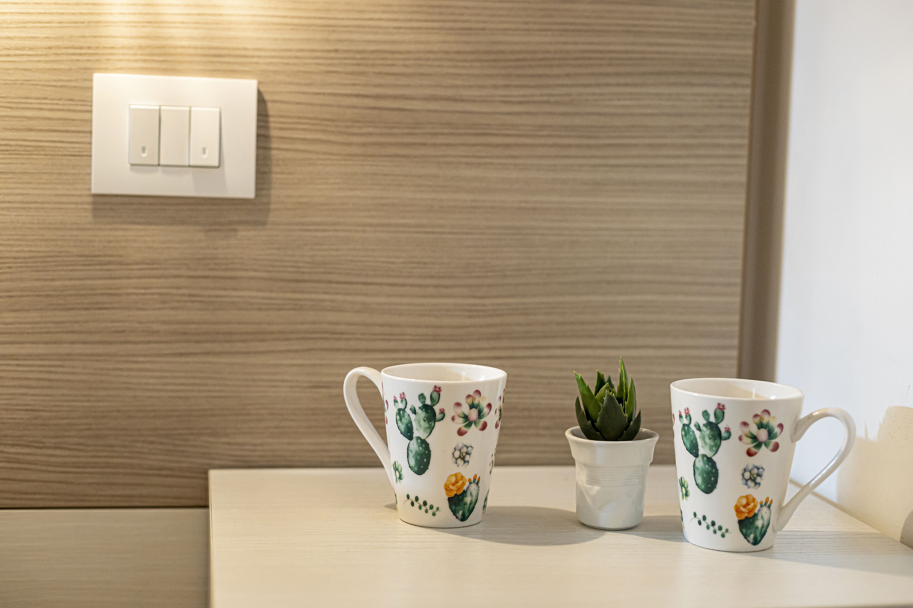Deux tasses en céramique blanche ornées de motifs de cactus, posées sur une surface en bois.