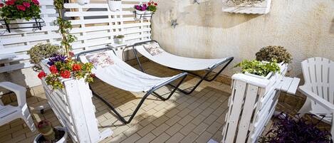 A patio with a hammock, white chairs, and potted plants.