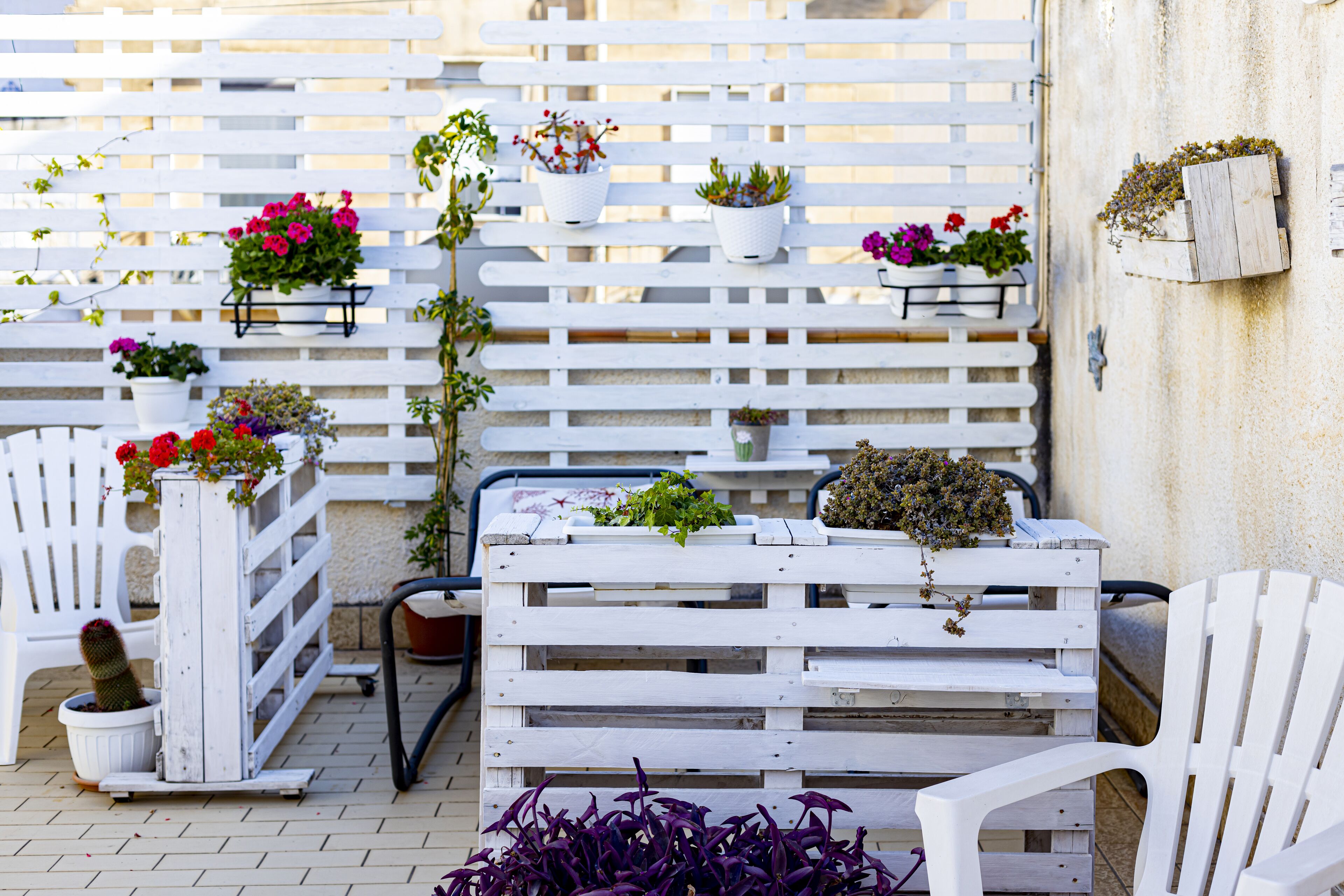 A patio area with white furniture, including a bench and chairs, and various potted plants.