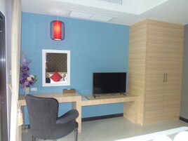 A room with a blue wall, a wooden desk with a TV, a chair, and a decorative vase with flowers.