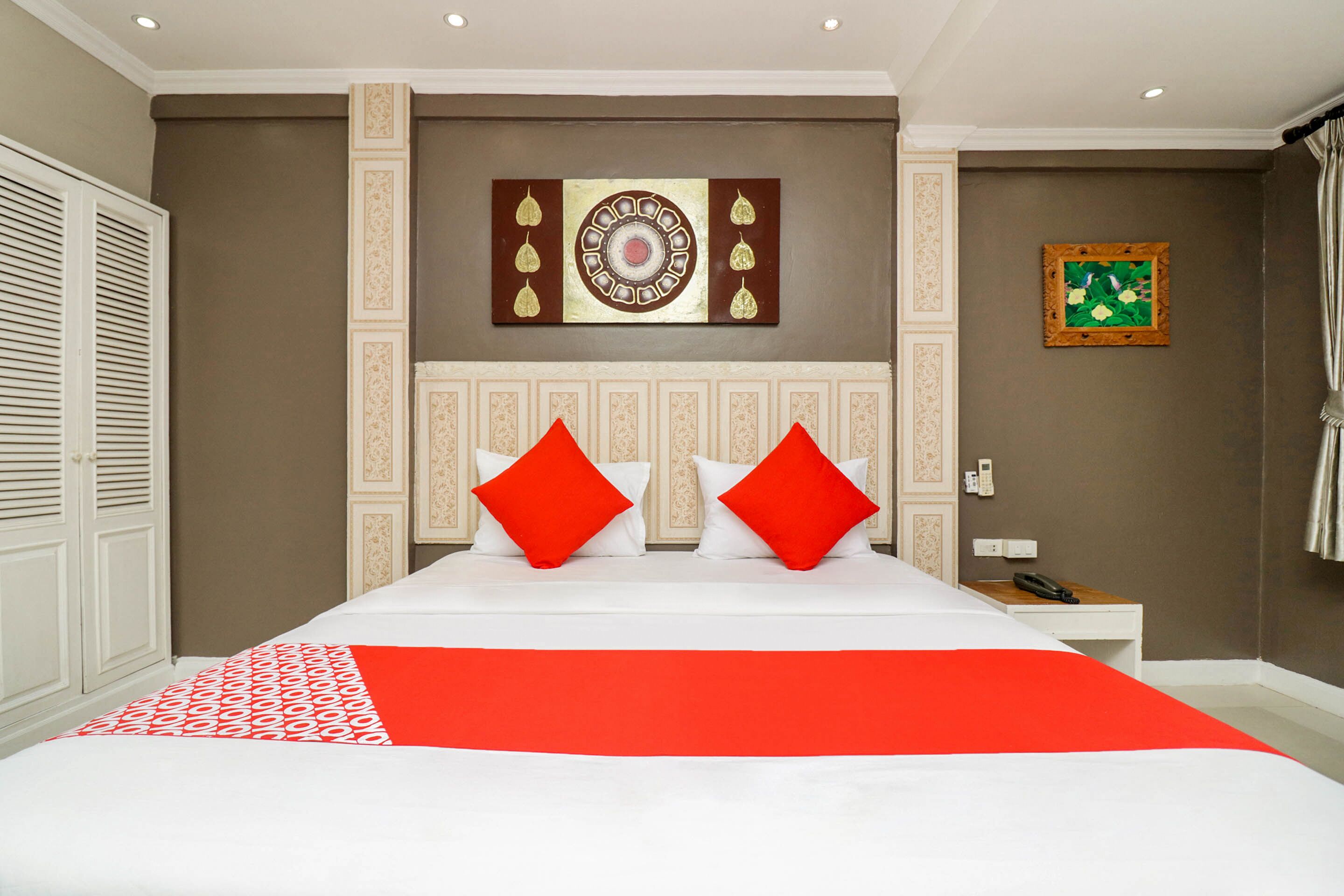 A hotel room with a large bed, two red pillows, a white bedside table, and a telephone.