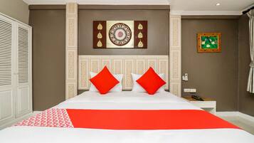 A hotel room with a large bed, two red pillows, a white bedside table, and a telephone.