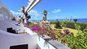 A balcony with a view of the sea, a white building, and a garden with various plants. - Hotel Albatros (Forio)