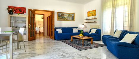 A living room with a blue sofa set, a wooden coffee table, and a dining area with a table and chairs.