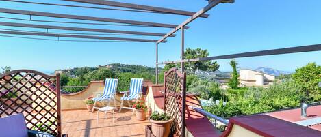 A terrace with two blue-striped lounge chairs, a wicker sofa, and potted plants.
