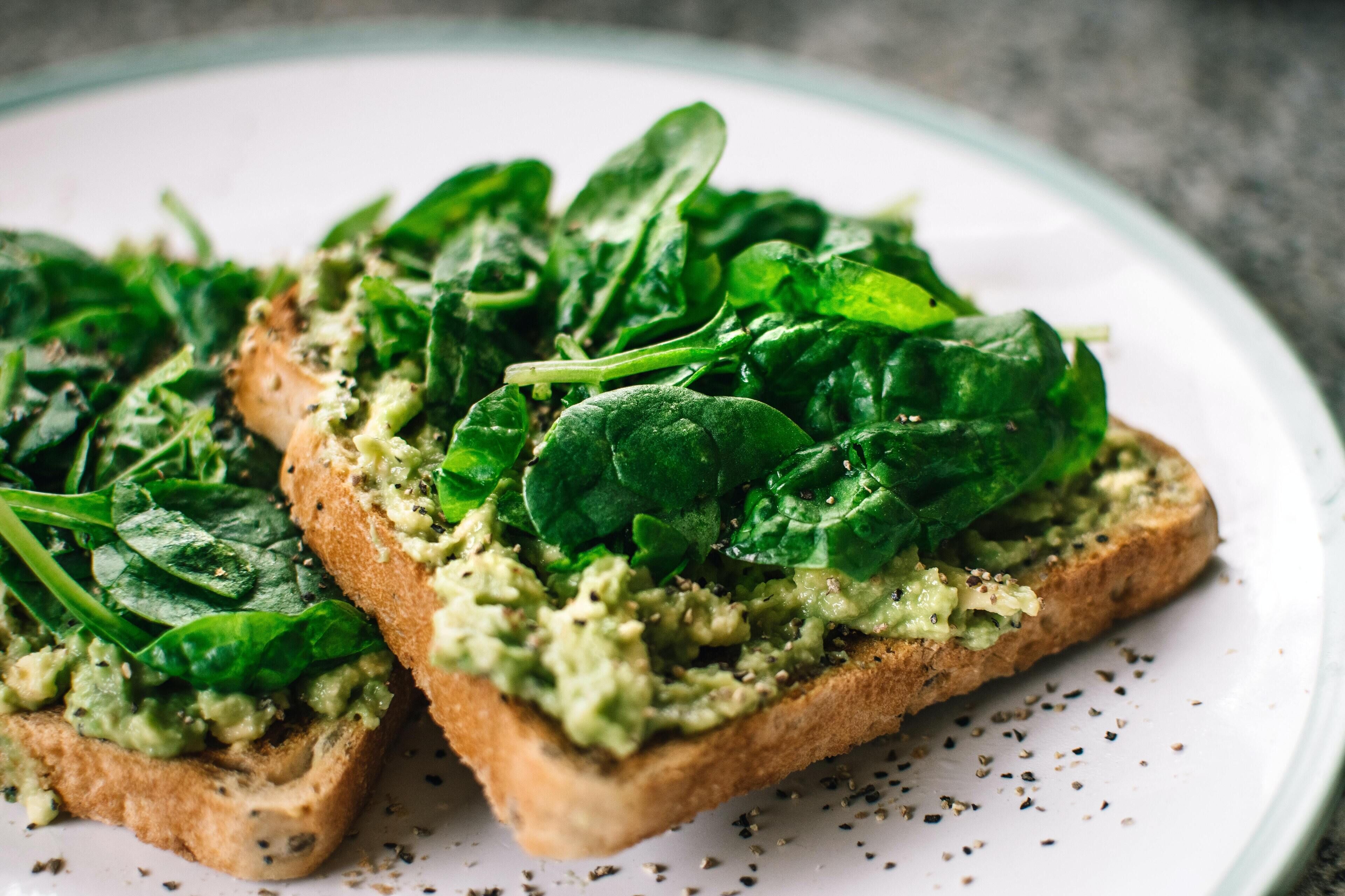 Two slices of toast topped with spinach and a green spread, possibly avocado, on a white plate.