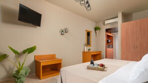 Habitación de hotel con cama, banco de madera, televisor montado en la pared, espejo y armario.