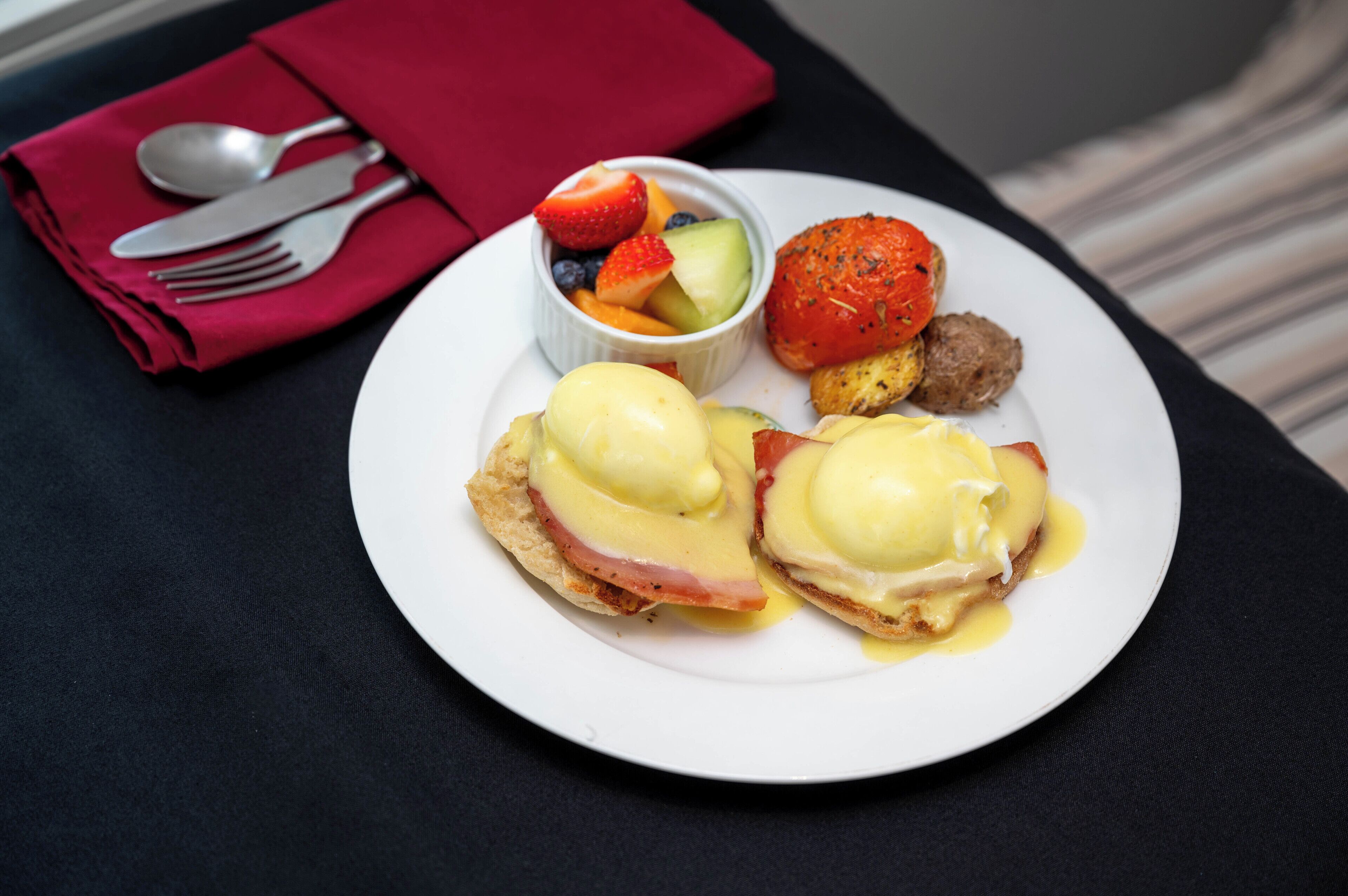 A plate with eggs benedict, a side of fruit, and a small portion of meat.