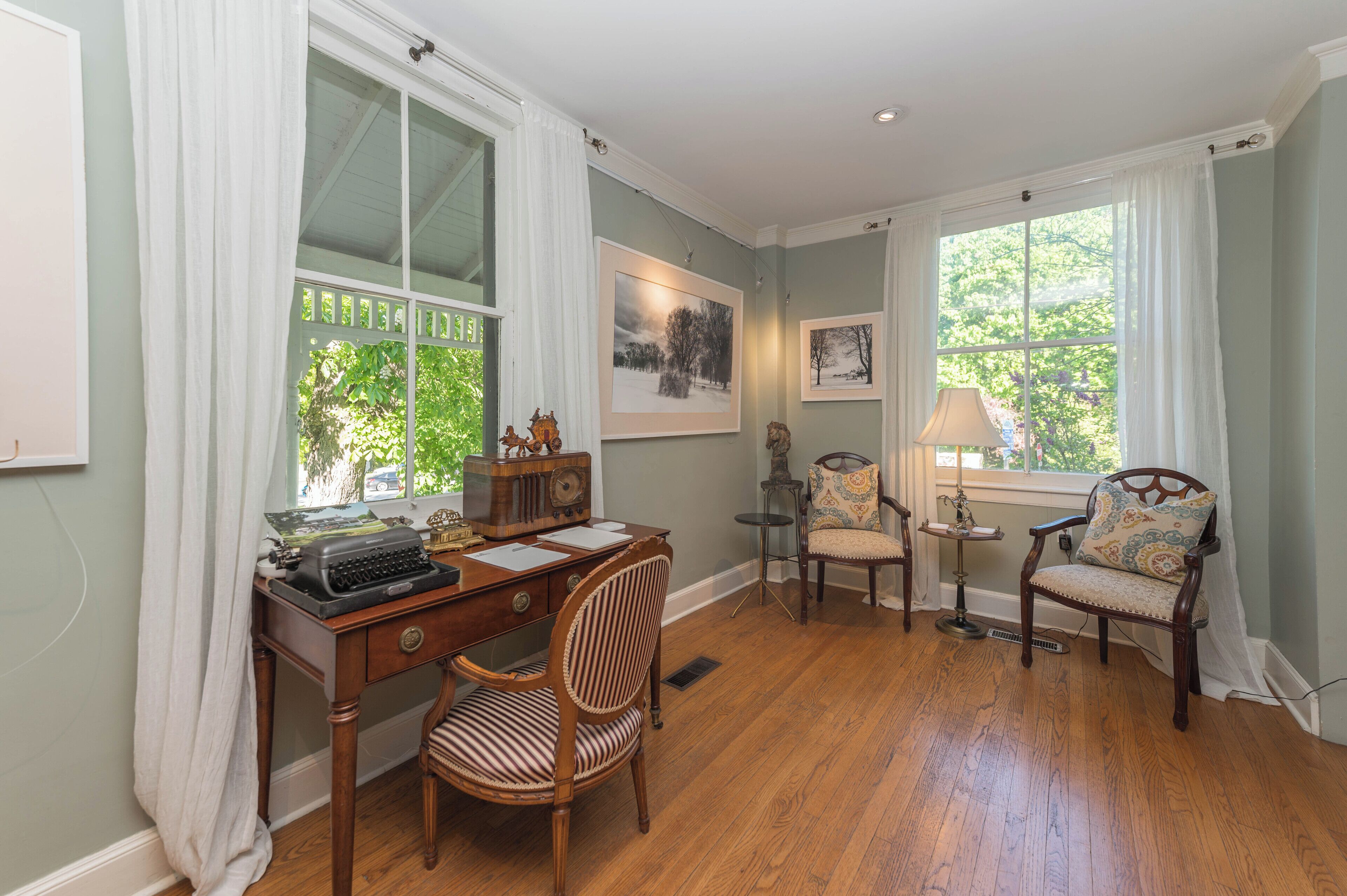 A room with a wooden desk, a chair, a lamp, and two framed pictures on the wall.