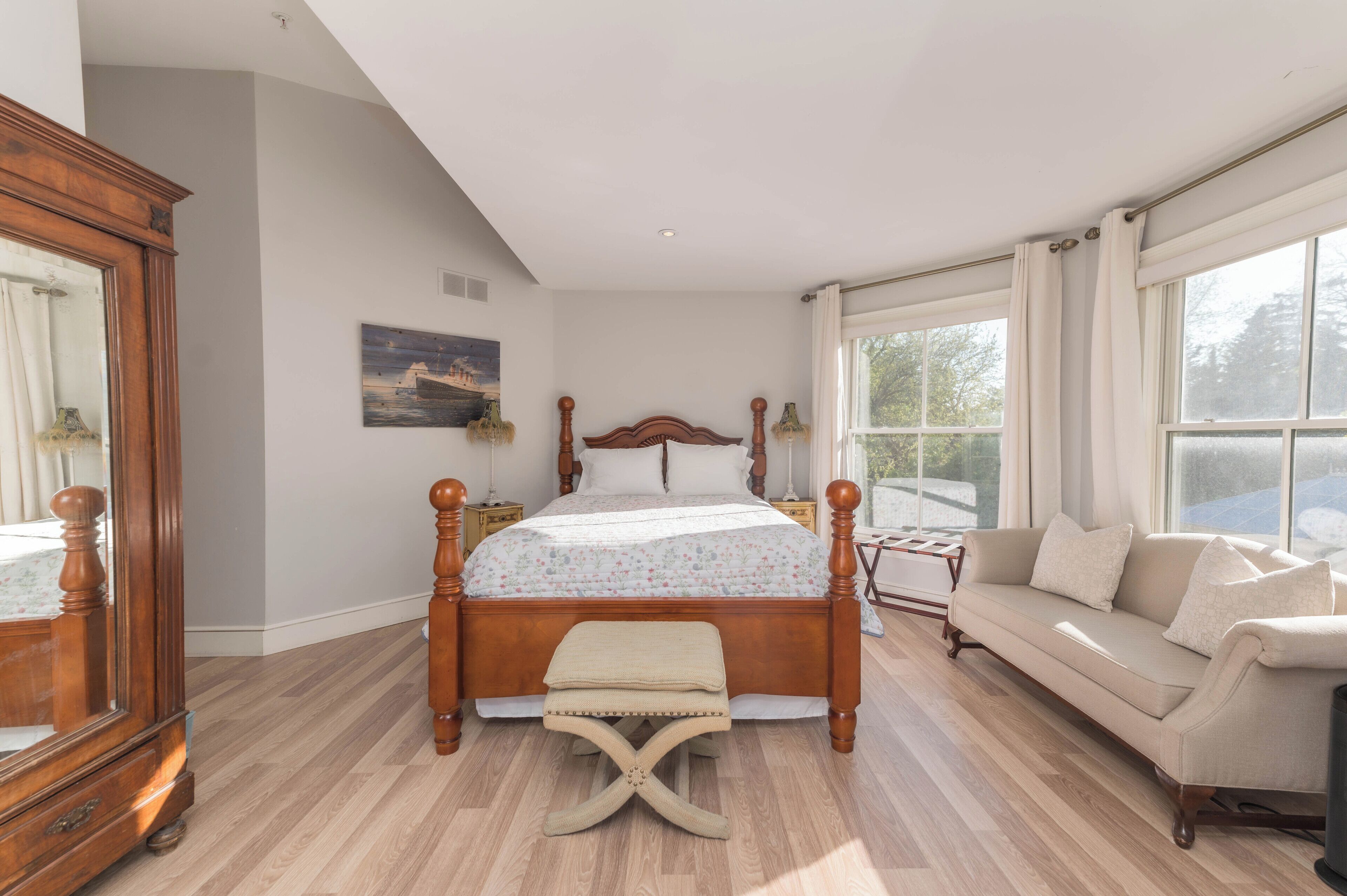 Un dormitorio con una cama con dosel de madera, un sofá, un espejo grande y un cuadro en la pared.