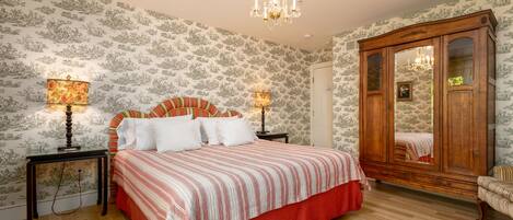 Un dormitorio con una cama grande, dos mesitas de noche con lámparas, un armario de madera y un papel pintado con estampado.