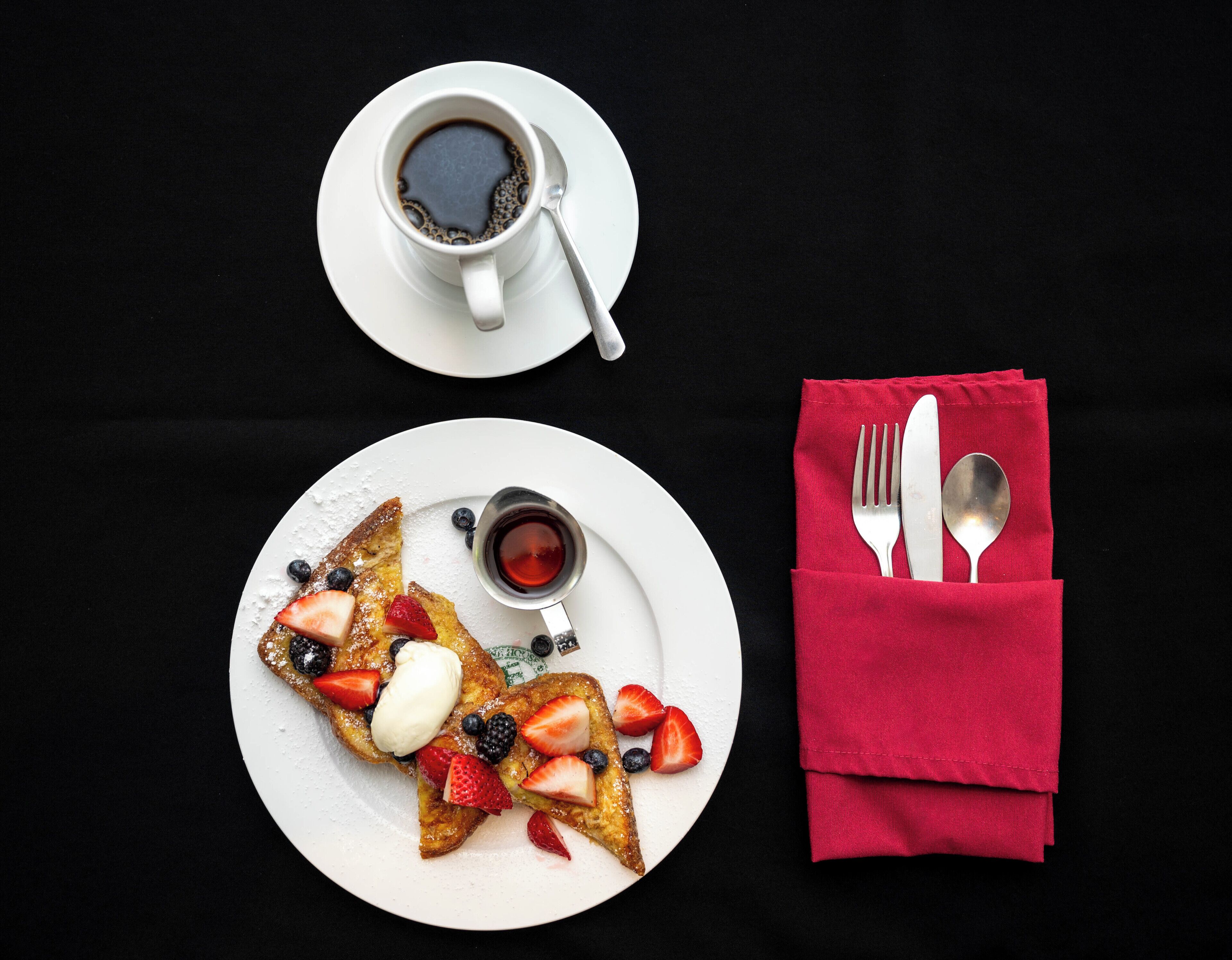 A breakfast setting with toast, strawberries, blueberries, and a cup of coffee on a black table.