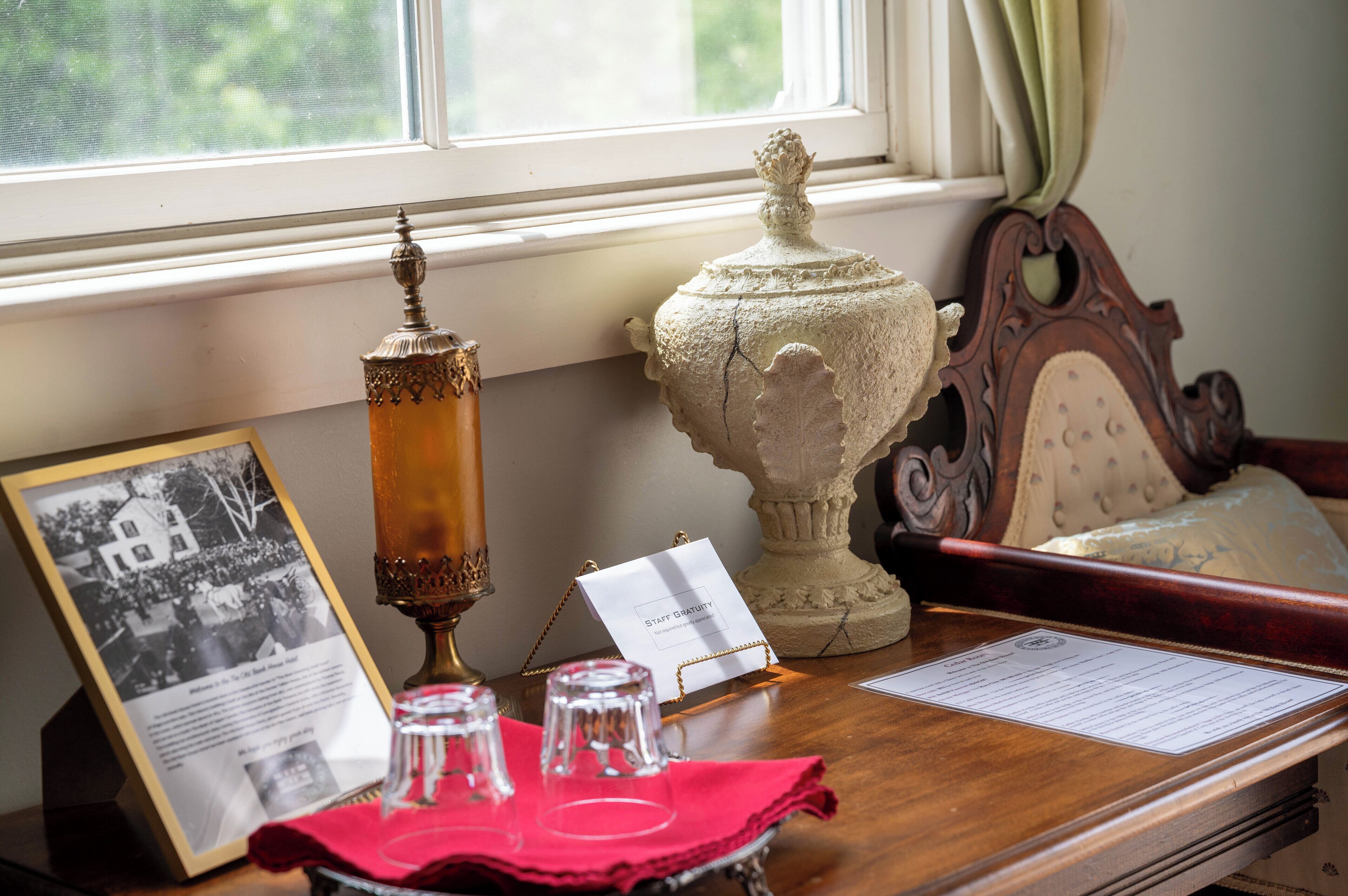 A table with a framed historical photo, a candle holder, a decorative urn, and a menu on a wooden table near a window.