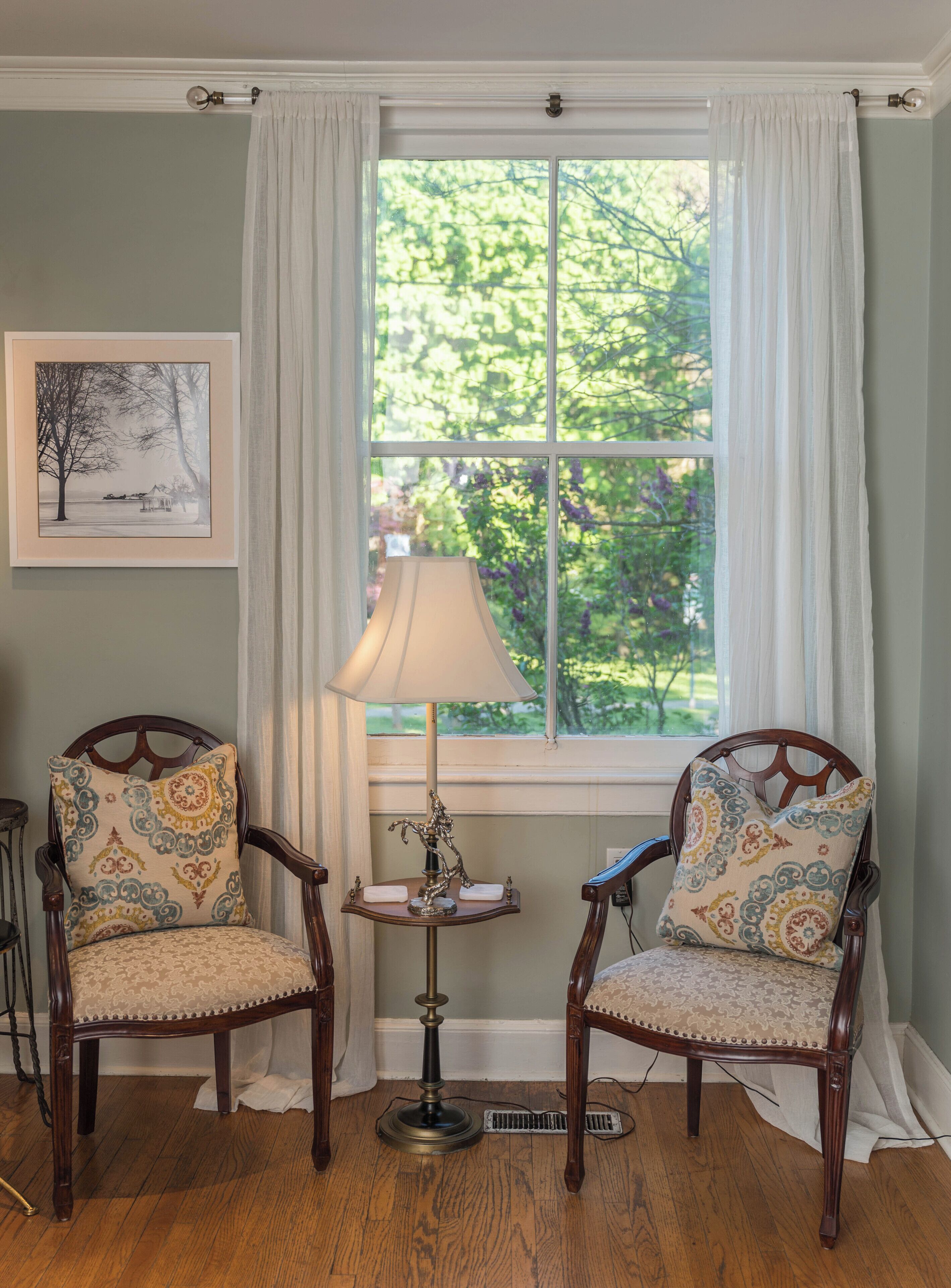 A room with two wooden chairs with patterned cushions, a floor lamp, and a framed picture on the wall.