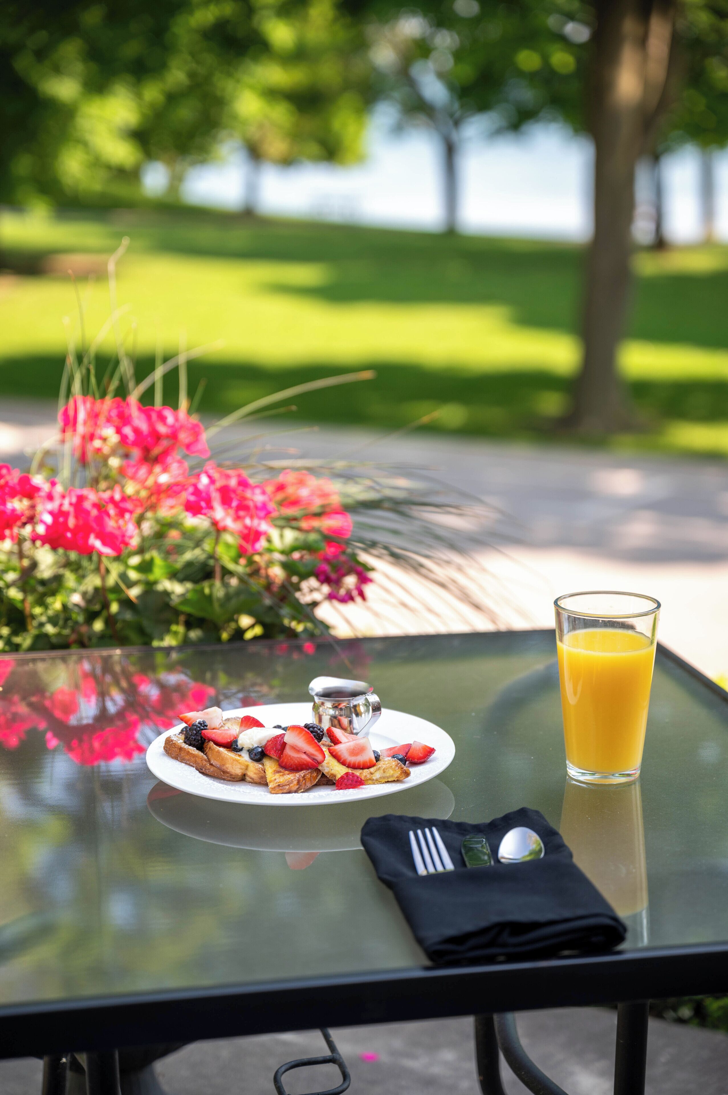 A glass table with a plate of food, a glass of orange juice, and a napkin with utensils.