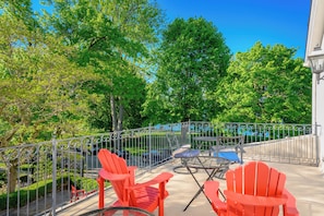 An outdoor patio with red Adirondack chairs, a round table, and a metal fence. - The Old Bank House Bed & Breakfast (Niagara-on-the-Lake)