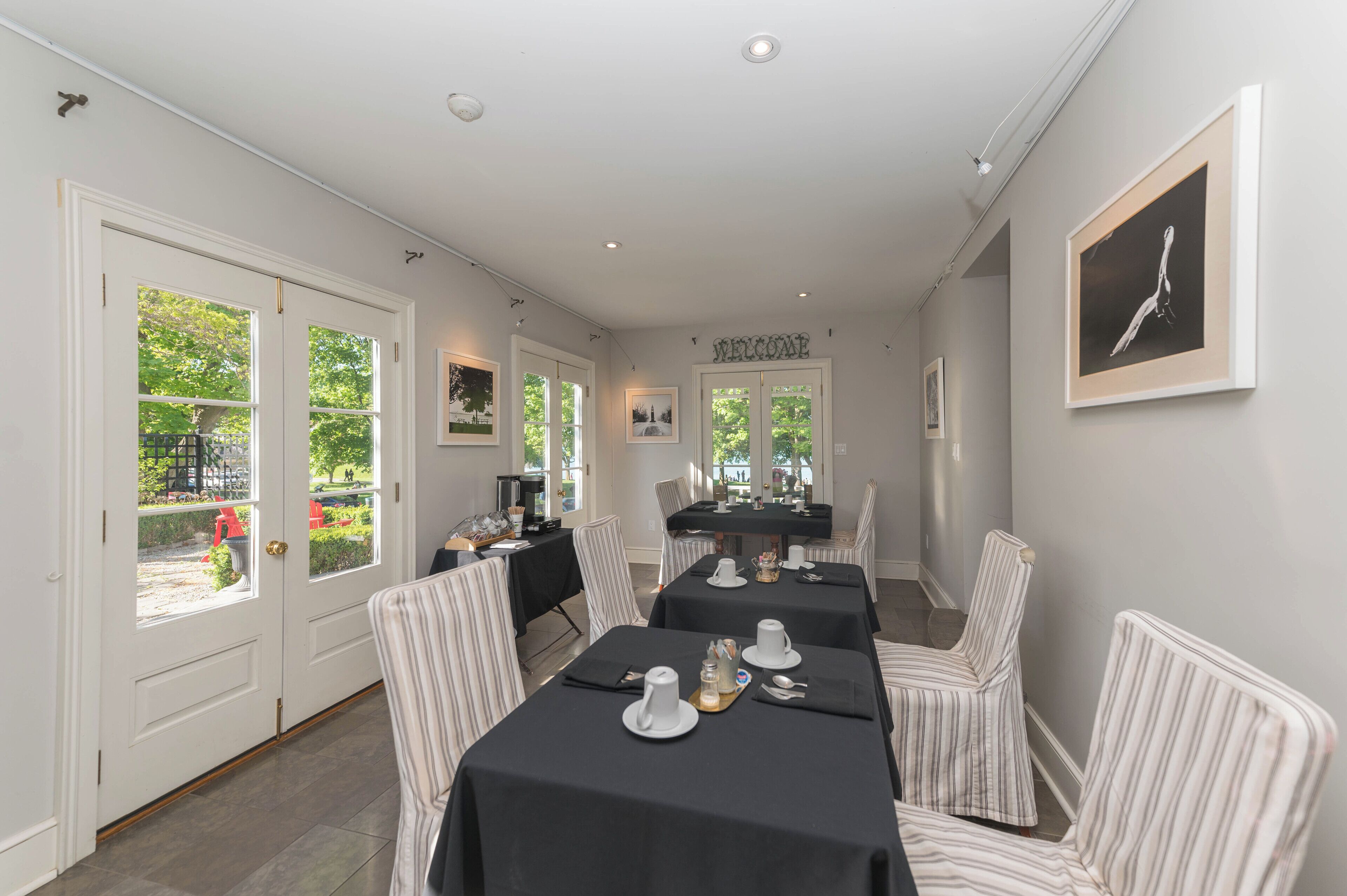 A dining area with tables set for four, striped chairs, and a 'WELCOME' sign on the wall.