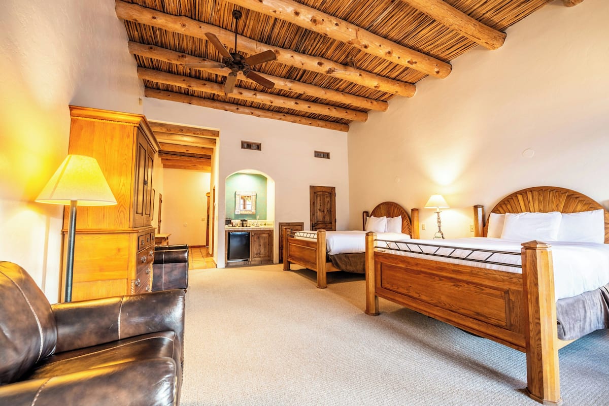 A room with a wooden ceiling, a bed, a desk, a chair, and a lamp.
