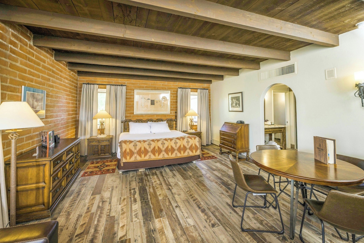 Habitación de hotel con techo de madera, cama grande, escritorio, silla y mesa de comedor.
