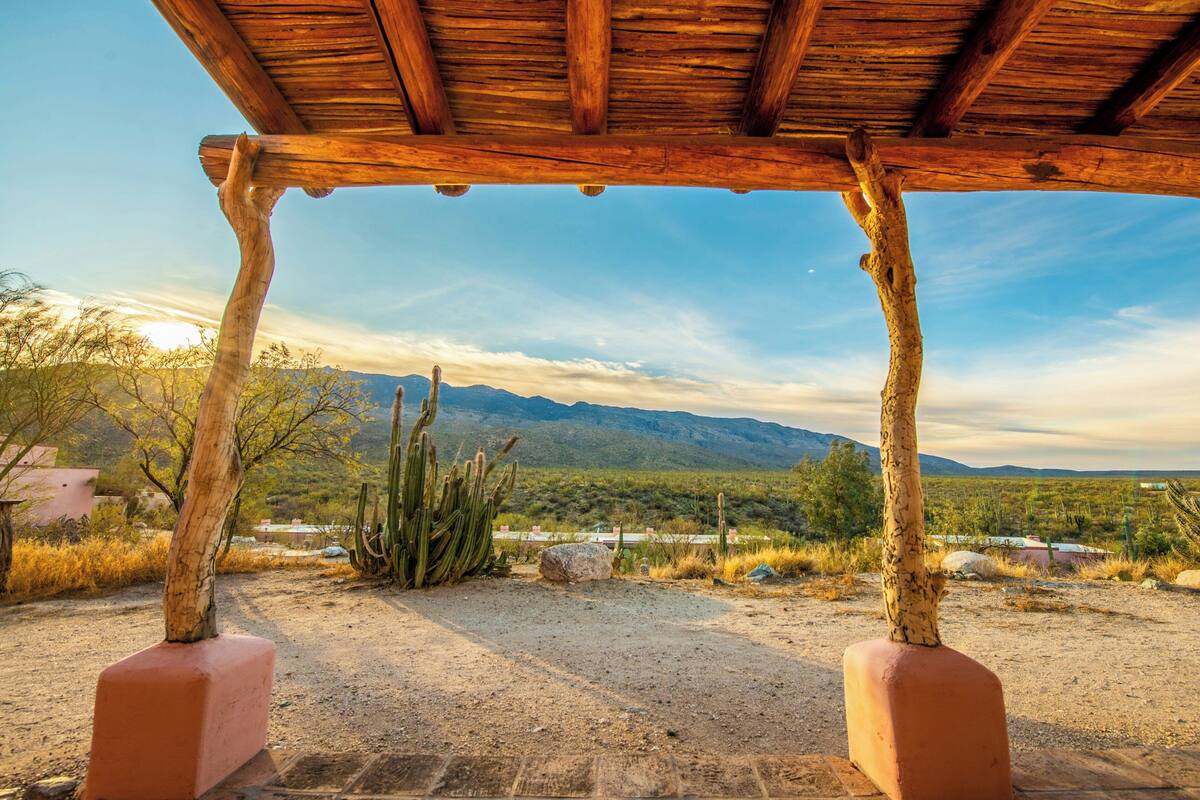 A wooden pergola structure with a view of a desert landscape and mountains in the background.