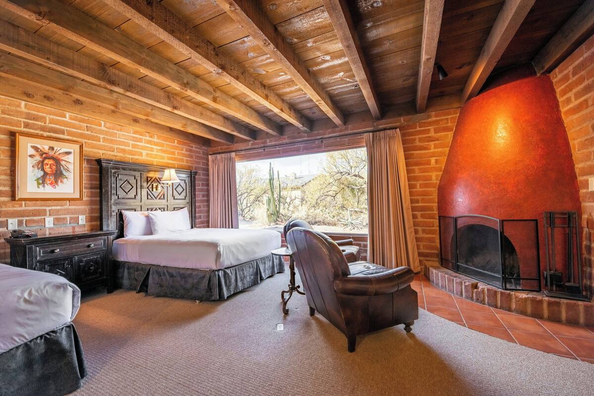 A rustic room with a brick fireplace, a bed, a desk, and a chair.