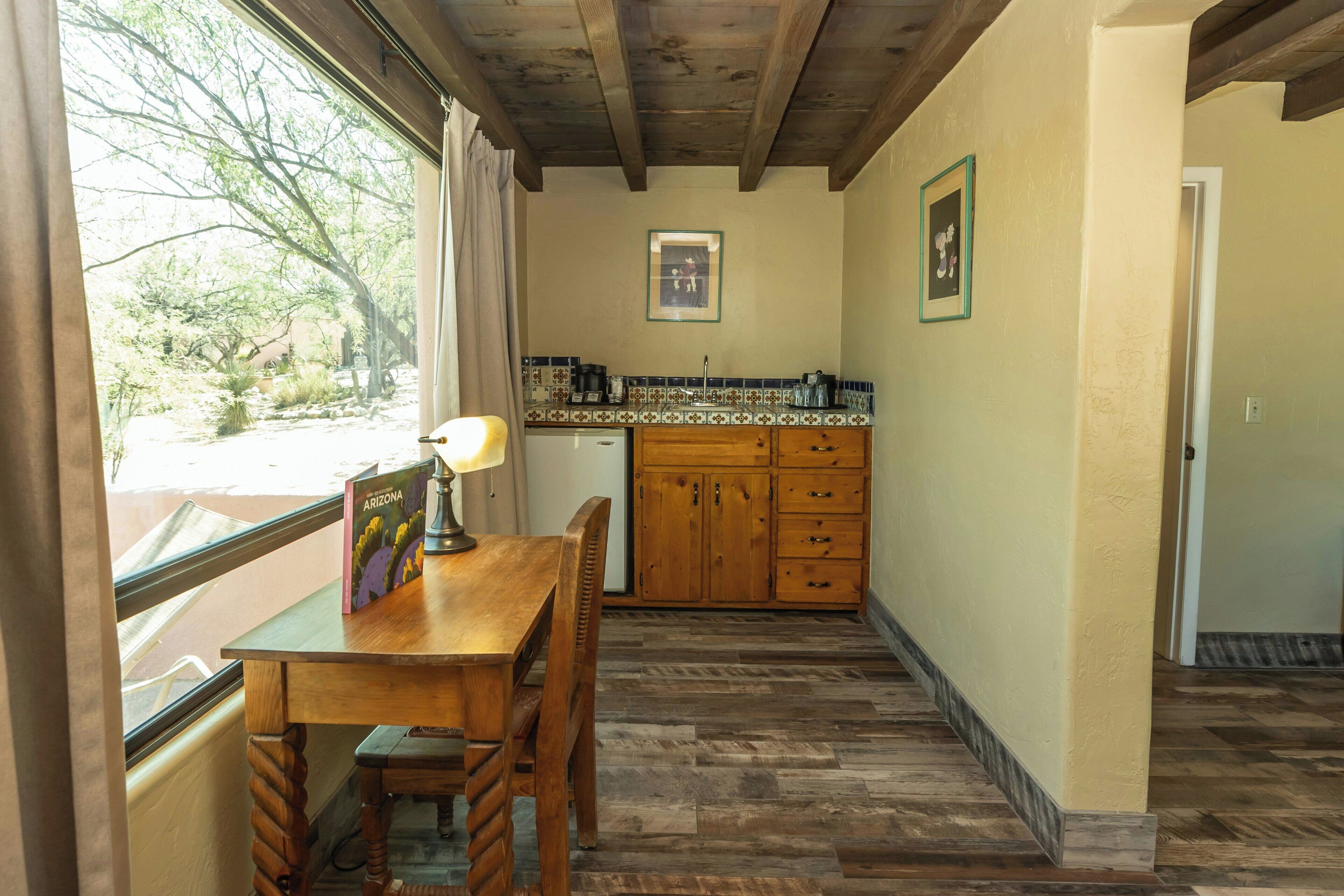 Een houten eettafel met stoelen, een keukenhoek met kastjes, en een raam met gordijnen.