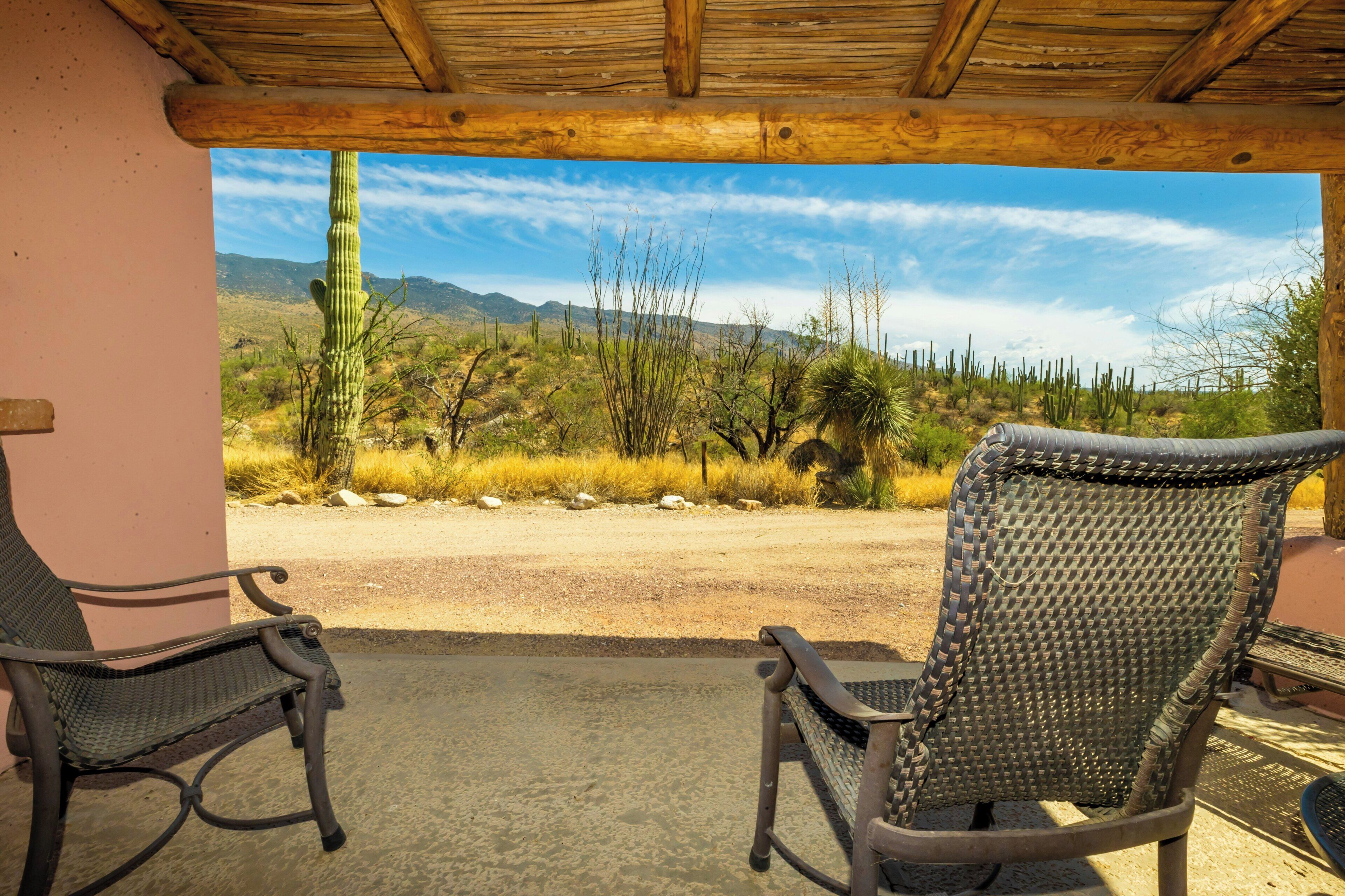 A patio with two rocking chairs facing a desert landscape with cacti and mountains.