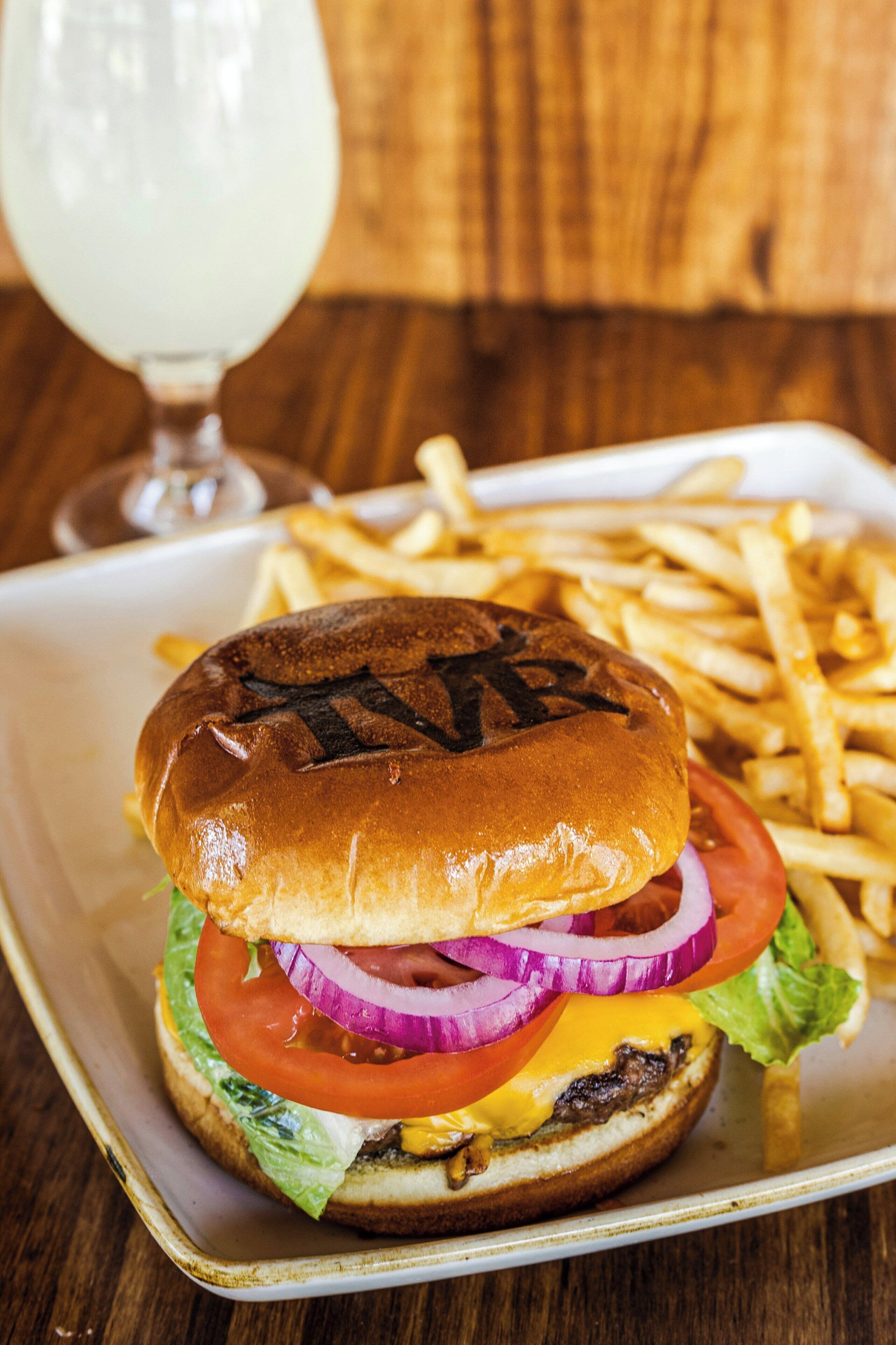 A sandwich with lettuce, tomato, onion, and cheese, accompanied by fries and a glass of a clear liquid.