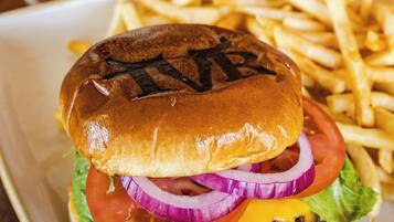 A sandwich with lettuce, tomato, onion, and cheese, accompanied by fries and a glass of a clear liquid.