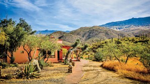 A desert landscape with a red building, a paved path, and sparse vegetation. - Tanque Verde Ranch (Tucson)