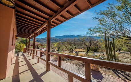 A covered outdoor area with a wooden railing, a view of desert vegetation, and distant mountains.
