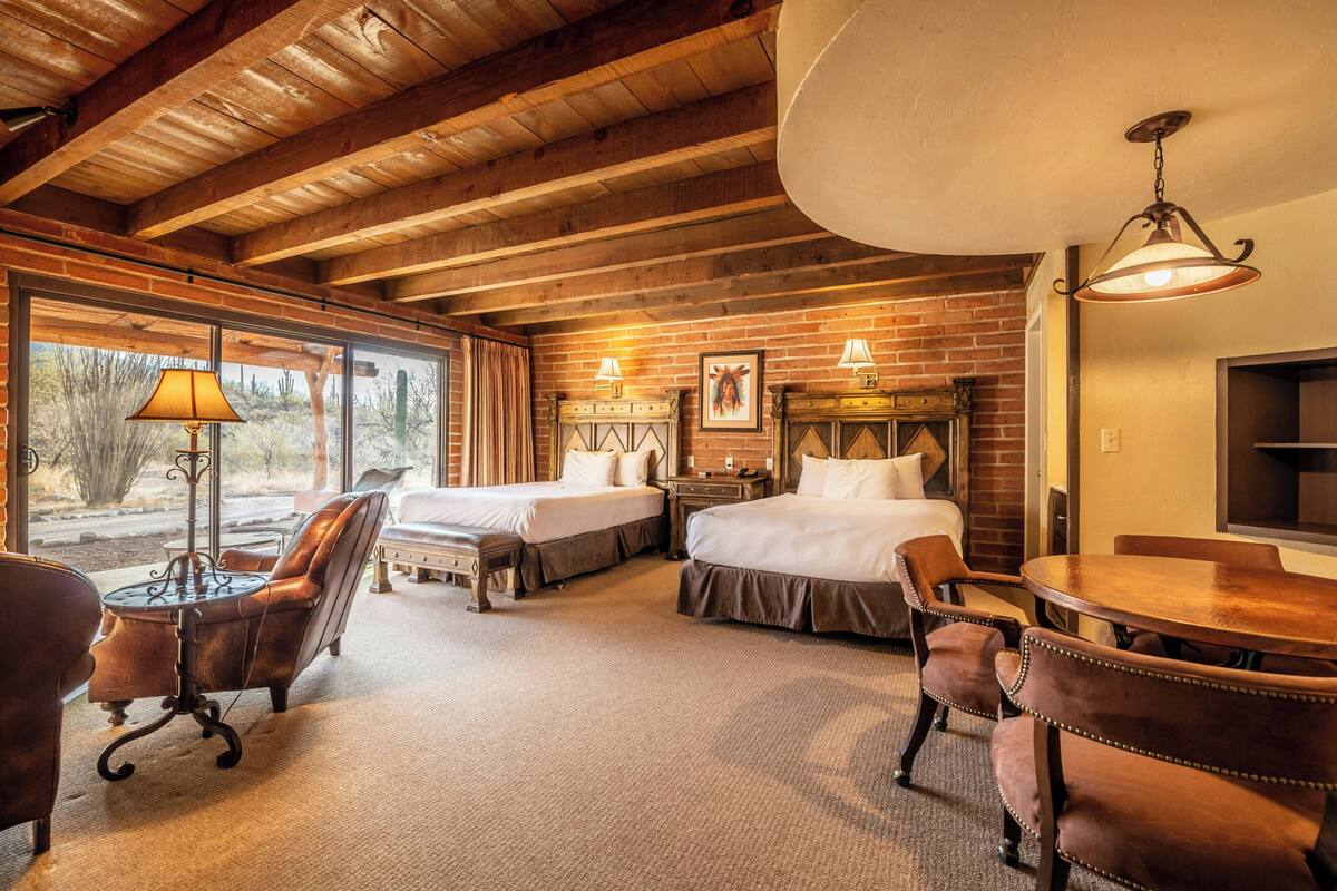 A room with two beds, a dining table, chairs, a lamp, and a TV.
