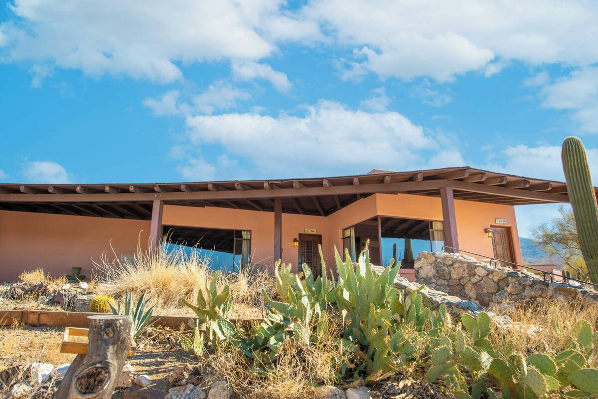 A building with a covered patio, a stone wall, and cacti in the foreground.