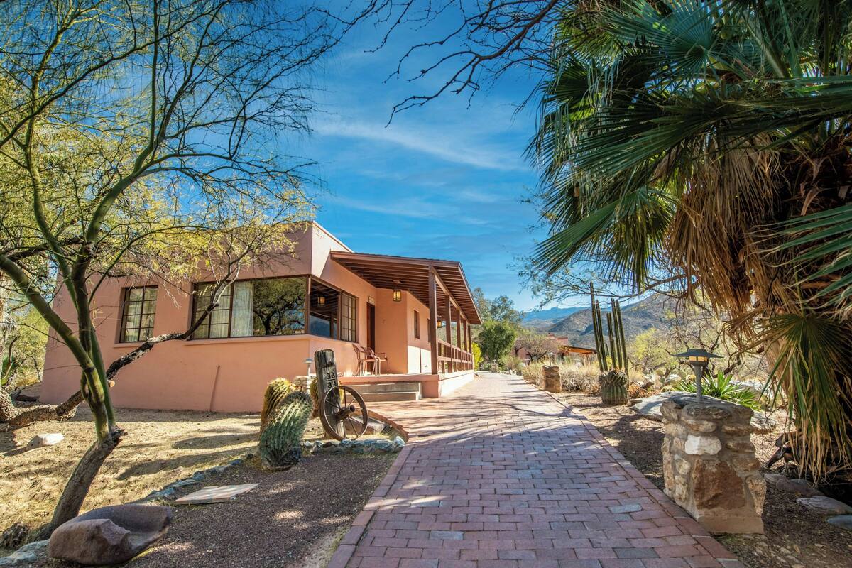 A building with a brick pathway leading to a wooden deck, surrounded by desert vegetation and cacti.