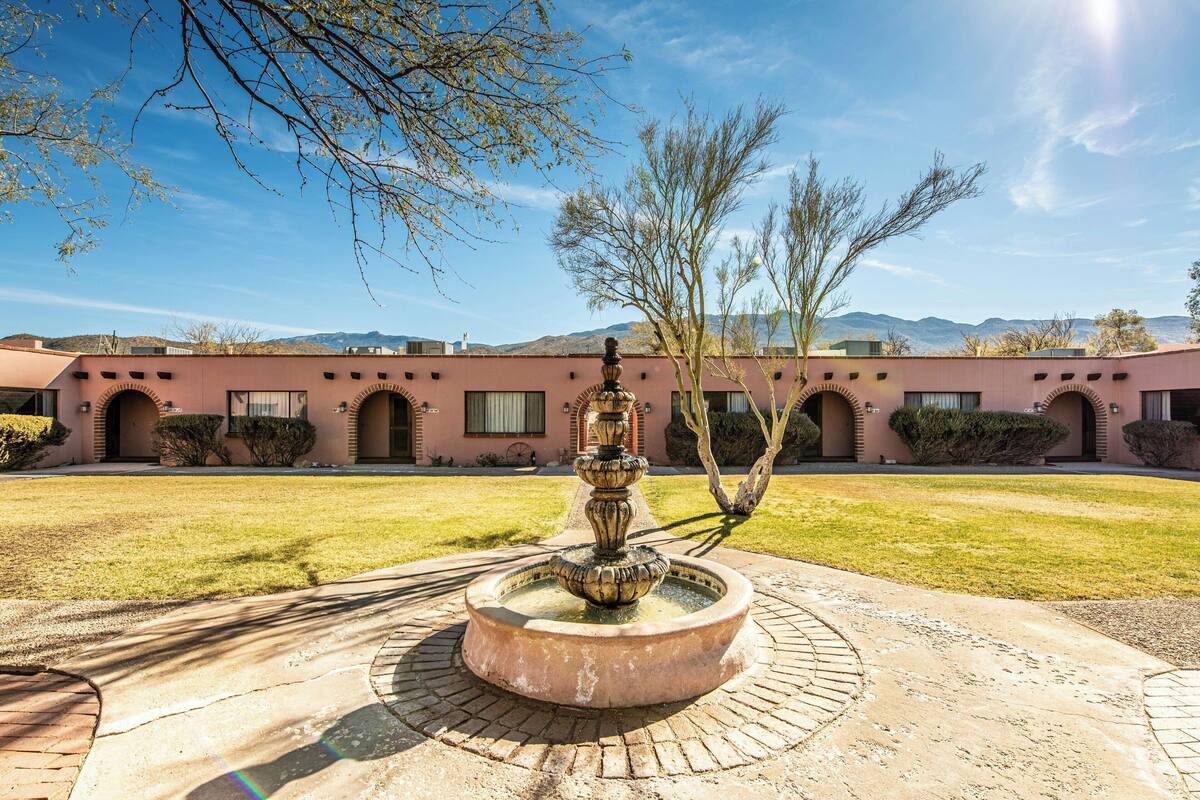 A courtyard with a fountain, a building with arched windows, and a clear sky.