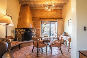 Una sala de estar acogedora con chimenea de piedra, sillones de cuero, una mesa redonda y vistas a través de un ventanal amplio.