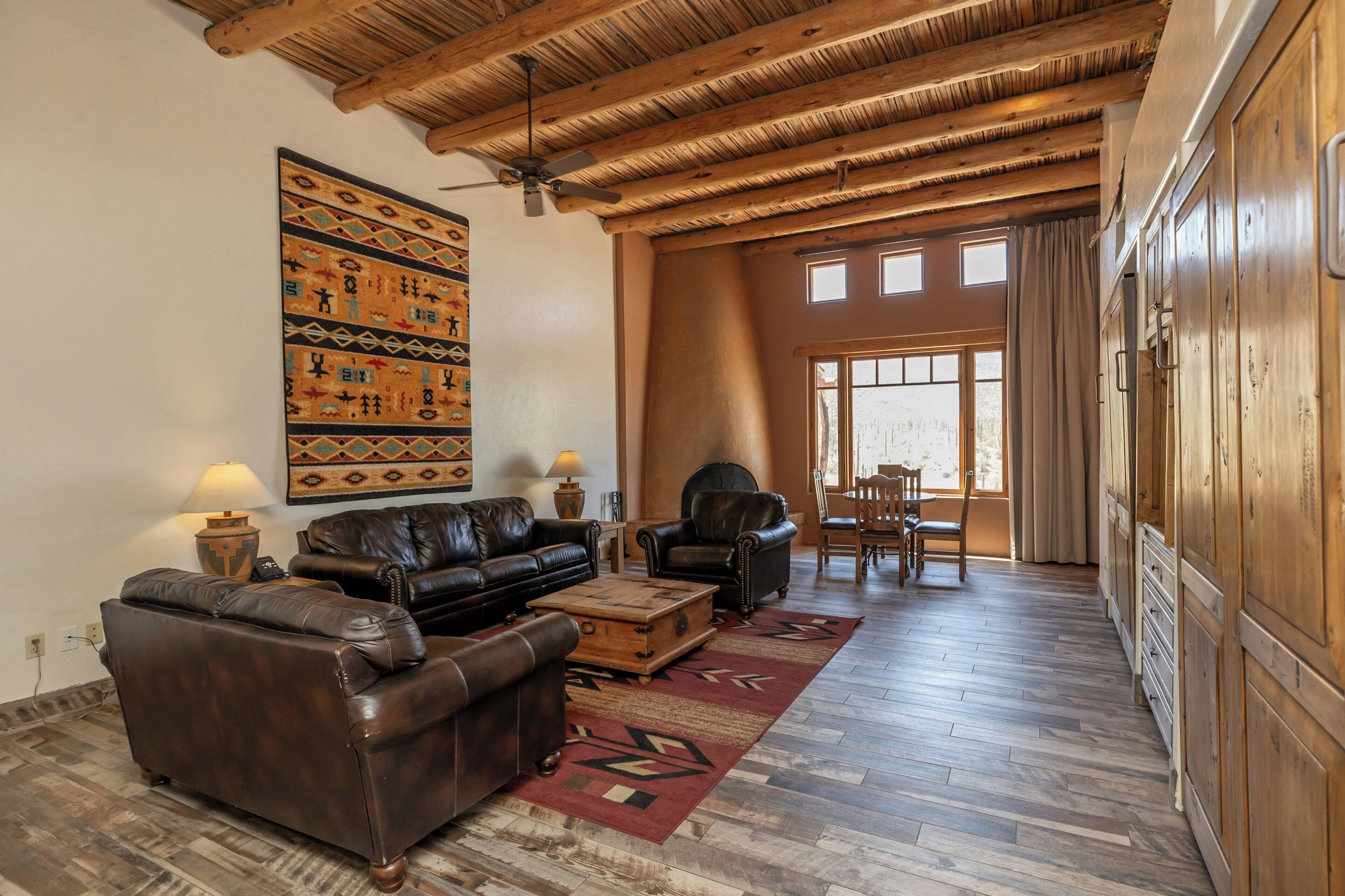 A spacious living room with a high ceiling, leather sofas, a coffee table, and a large wall rug.