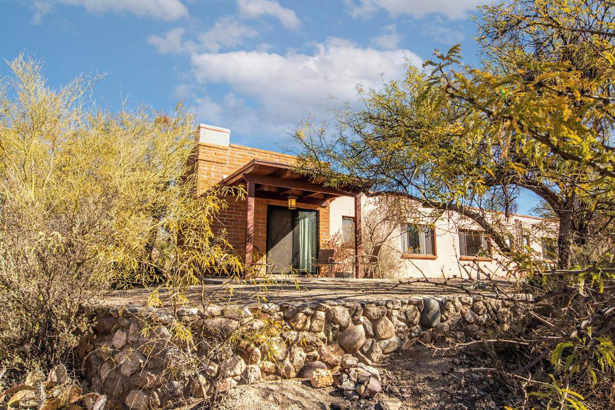 A rustic house with a stone wall, wooden porch, and a brick chimney.