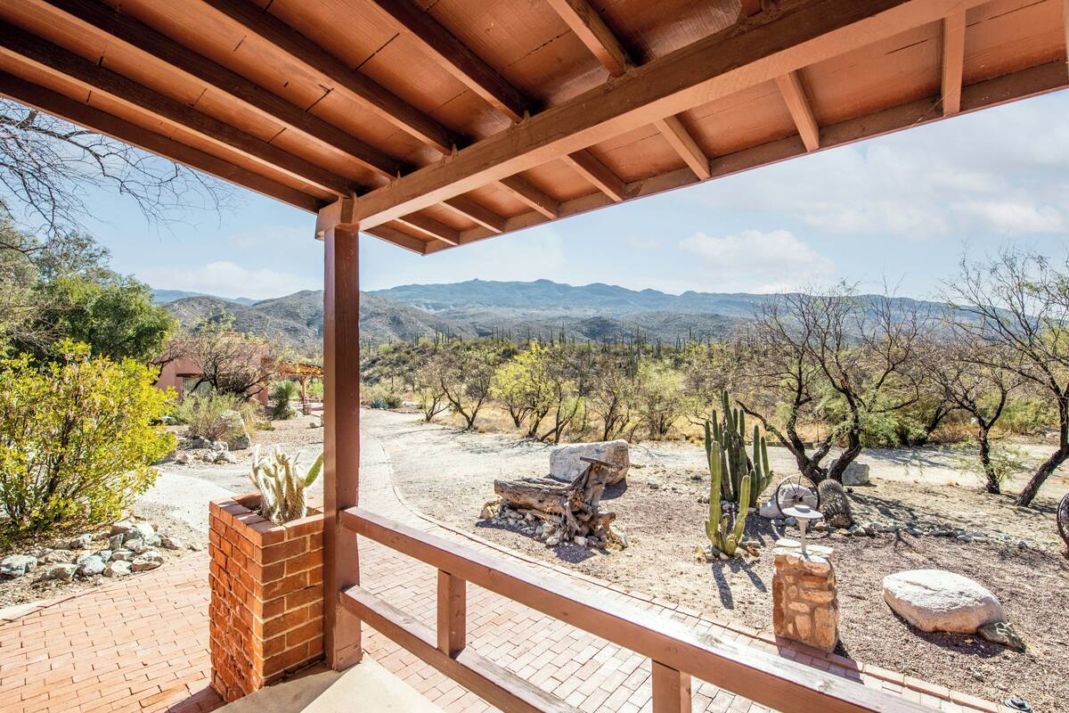 A covered patio with a view of a desert landscape, including cacti and distant mountains.