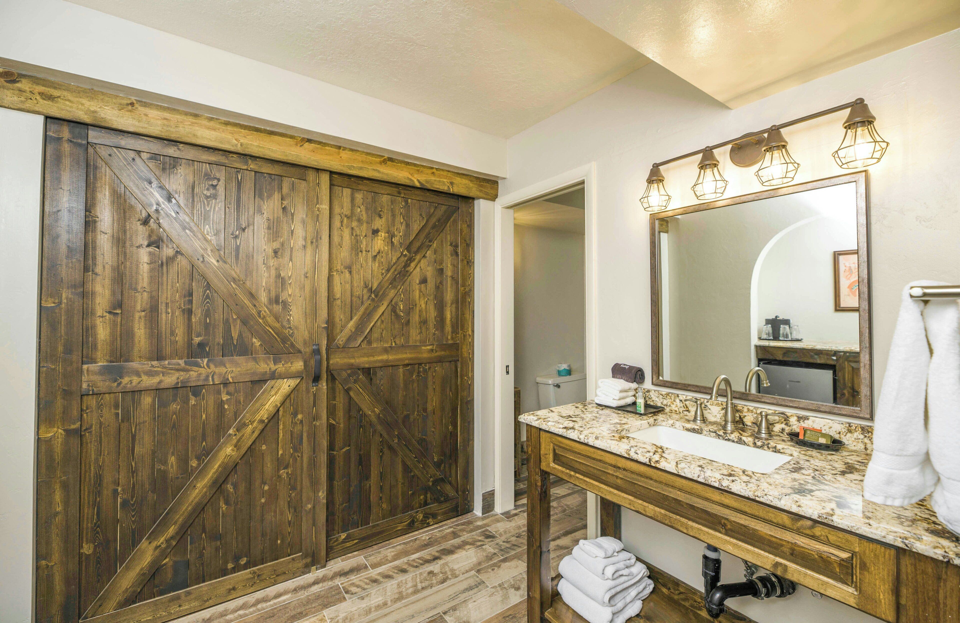 Un baño con puerta de madera, un lavamanos con espejo y un perchero para toallas.