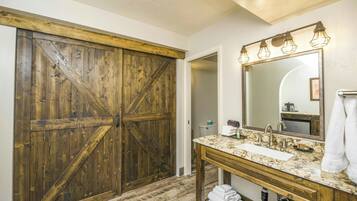 Un baño con puerta de madera, un lavamanos con espejo y un perchero para toallas.