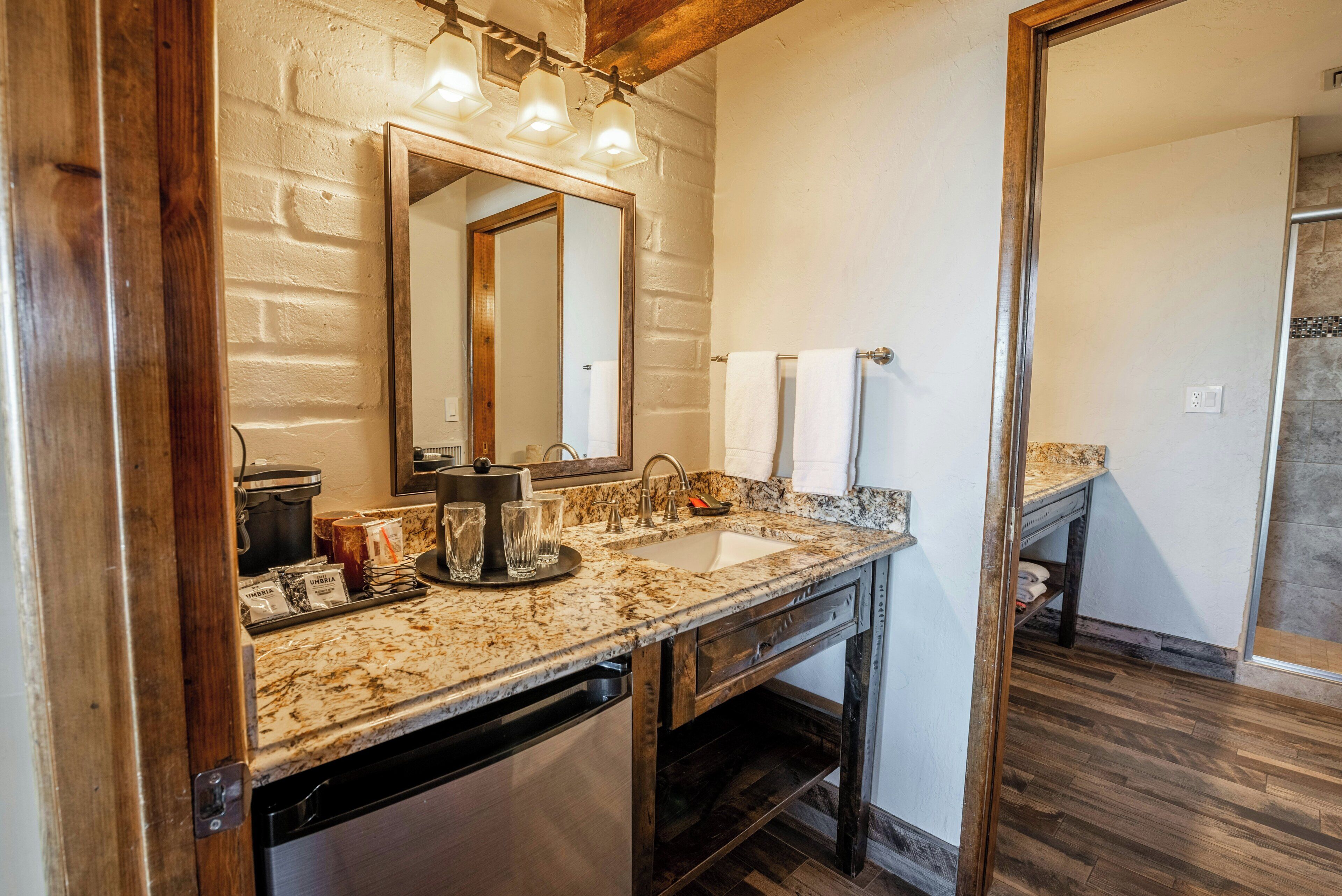 A bathroom with a granite countertop, a sink, a mirror, and a shower area.