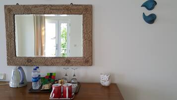 A mirror with a woven frame, a kettle, water bottles, a tray with snacks, and a white owl figurine on a wooden table.