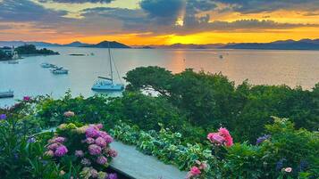 Vista costera con barcos, un velero y un jardín lleno de flores.
