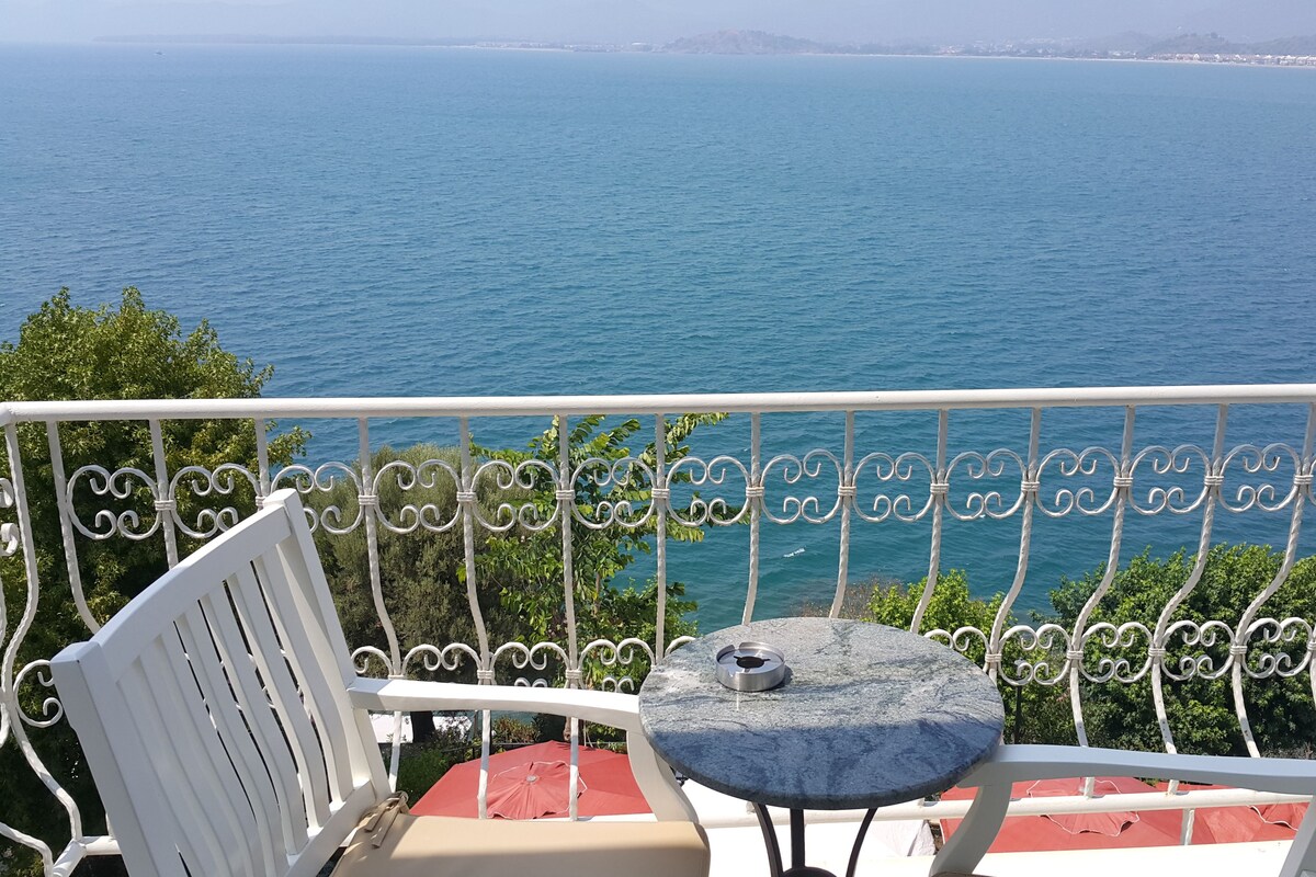A balcony with white metal railings, a round table with a cushion, and a red umbrella.