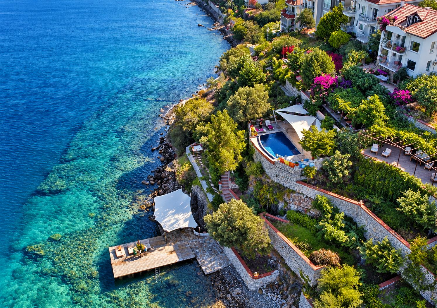 A coastal property with a swimming pool, stone walls, and lush greenery.